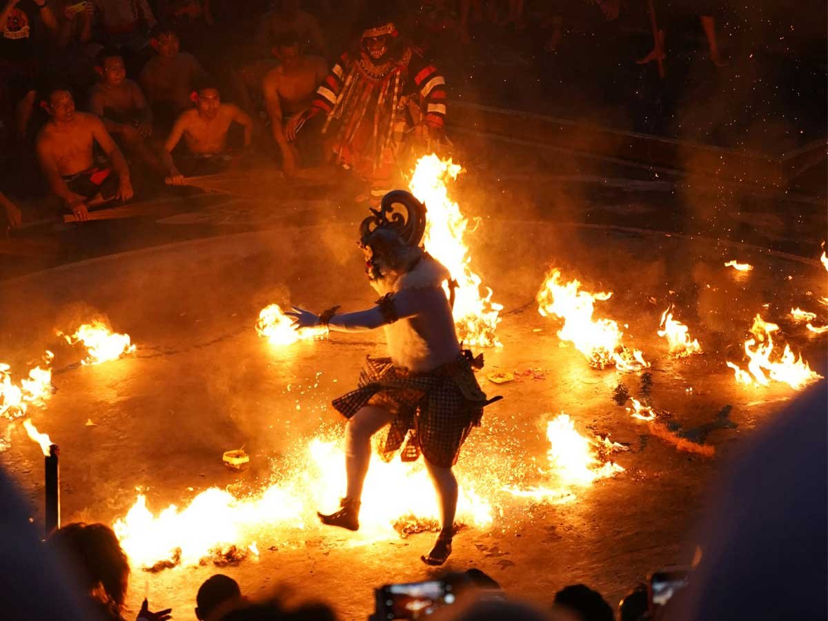 Masked monkey dancer in poleng cloth surrounded by chanting Kecak performers at night
